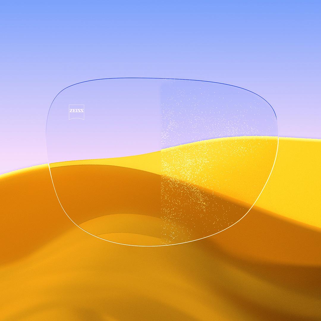 Ein Brillenglas im Vergleich: Eine Seite klar und sauber mit ZEISS DuraVision Gold UV, die andere Seite mit Staub bedeckt.