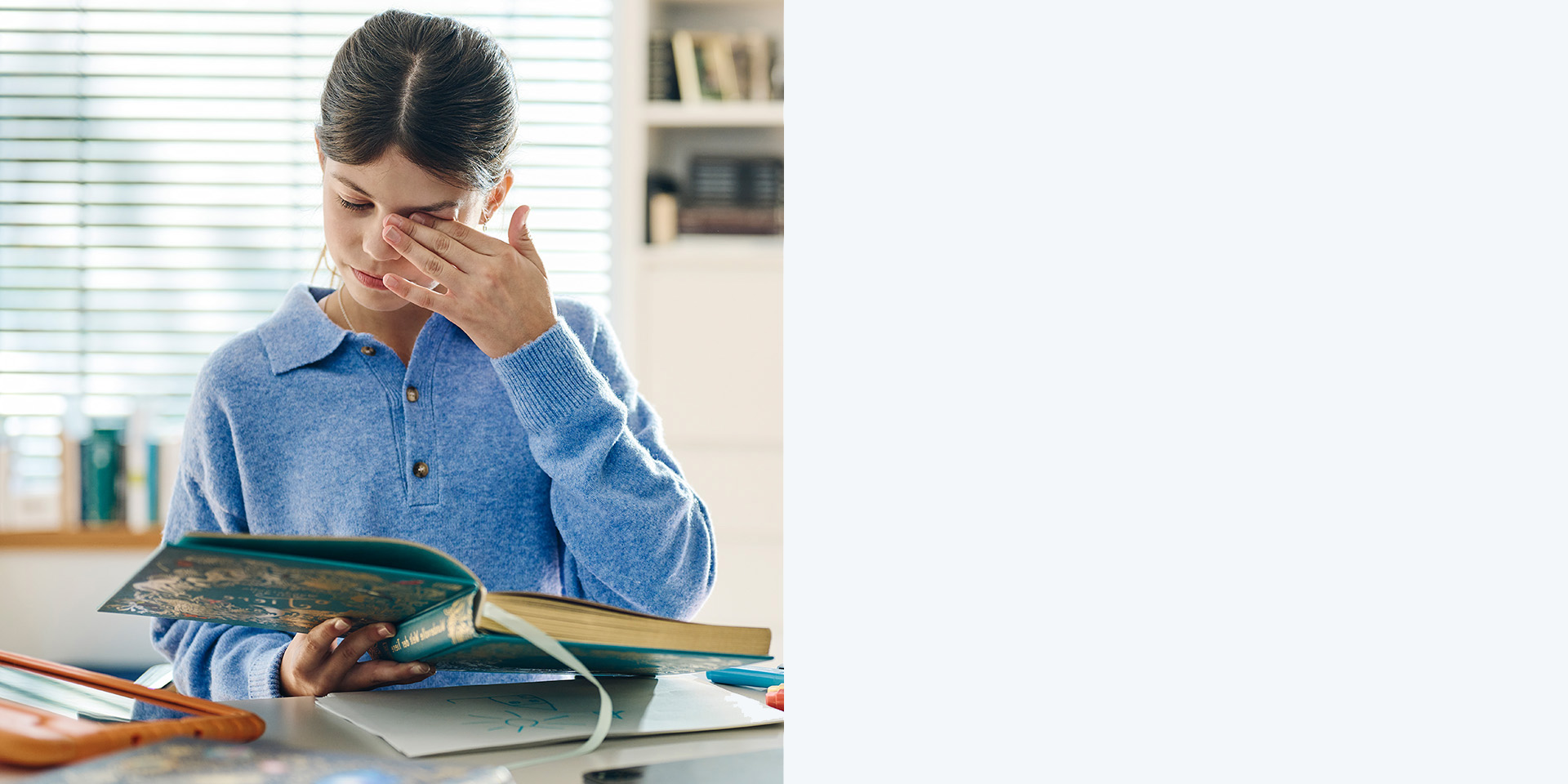 Jeune fille aux cheveux bruns sans lunettes qui se frotte les yeux en lisant un livre.