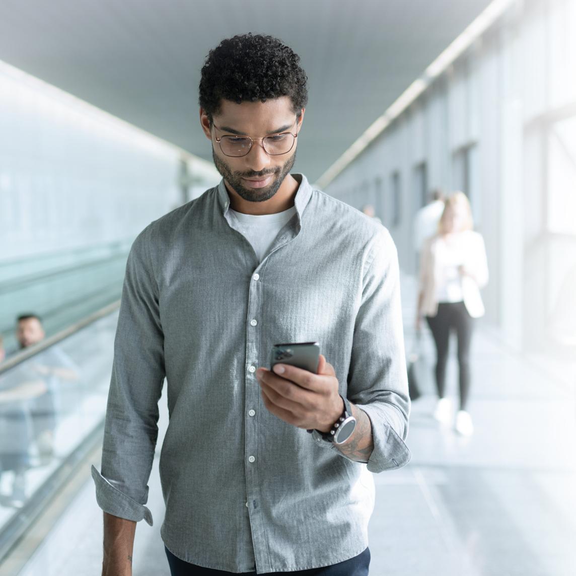 Ein junger Mann mit ZEISS SmartLife Brillengläsern schaut auf sein Telefon während er läuft.