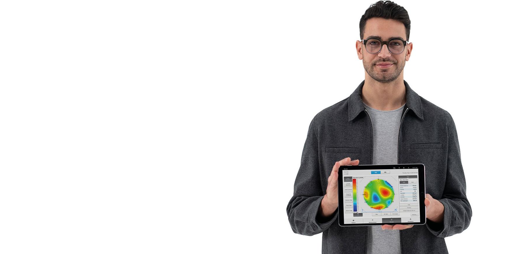 Un jeune homme porte des verres ZEISS et regarde droit dans l’appareil photo en tenant un iPad qui affiche les informations préalables pour une réfraction subjective précise.