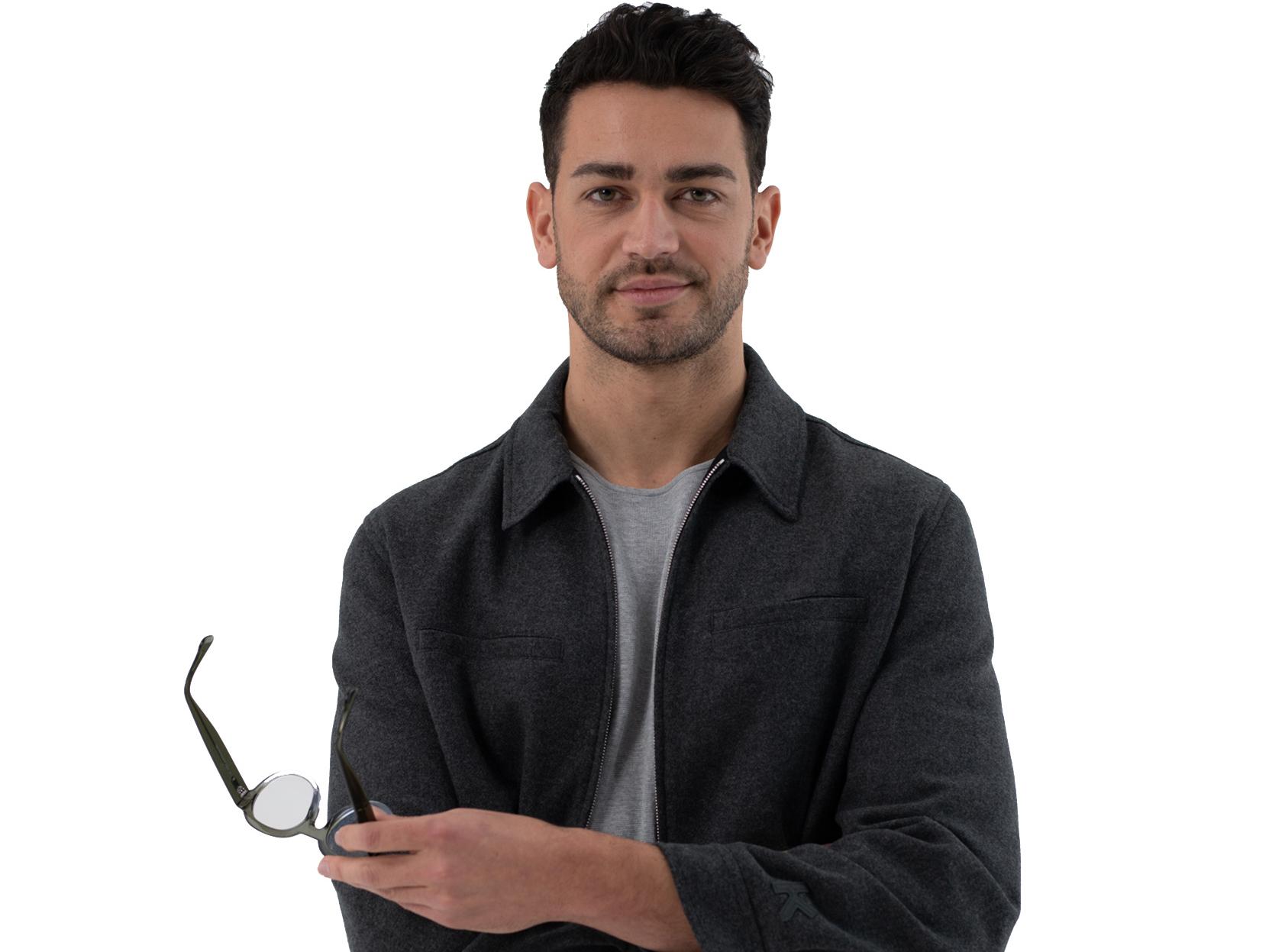 Jeune homme aux cheveux marrons et courts sourit pour la photo et tient des lunettes dans ses mains.