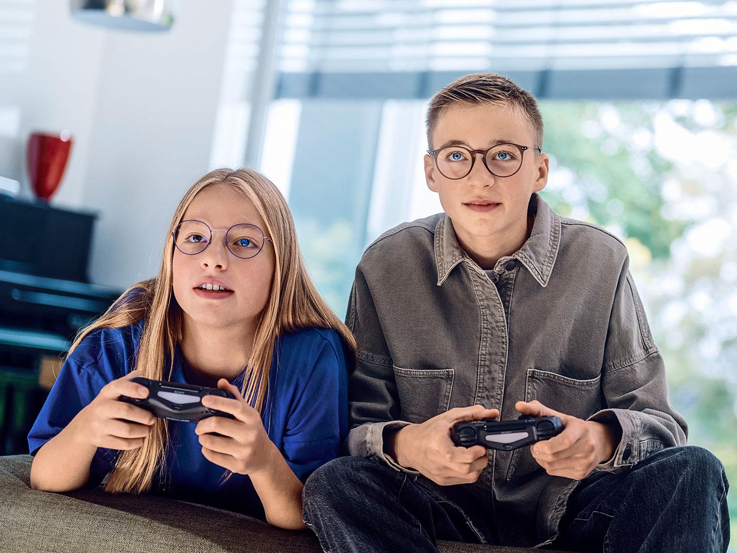 Deux adolescents jouent à des jeux vidéos avec des consoles.