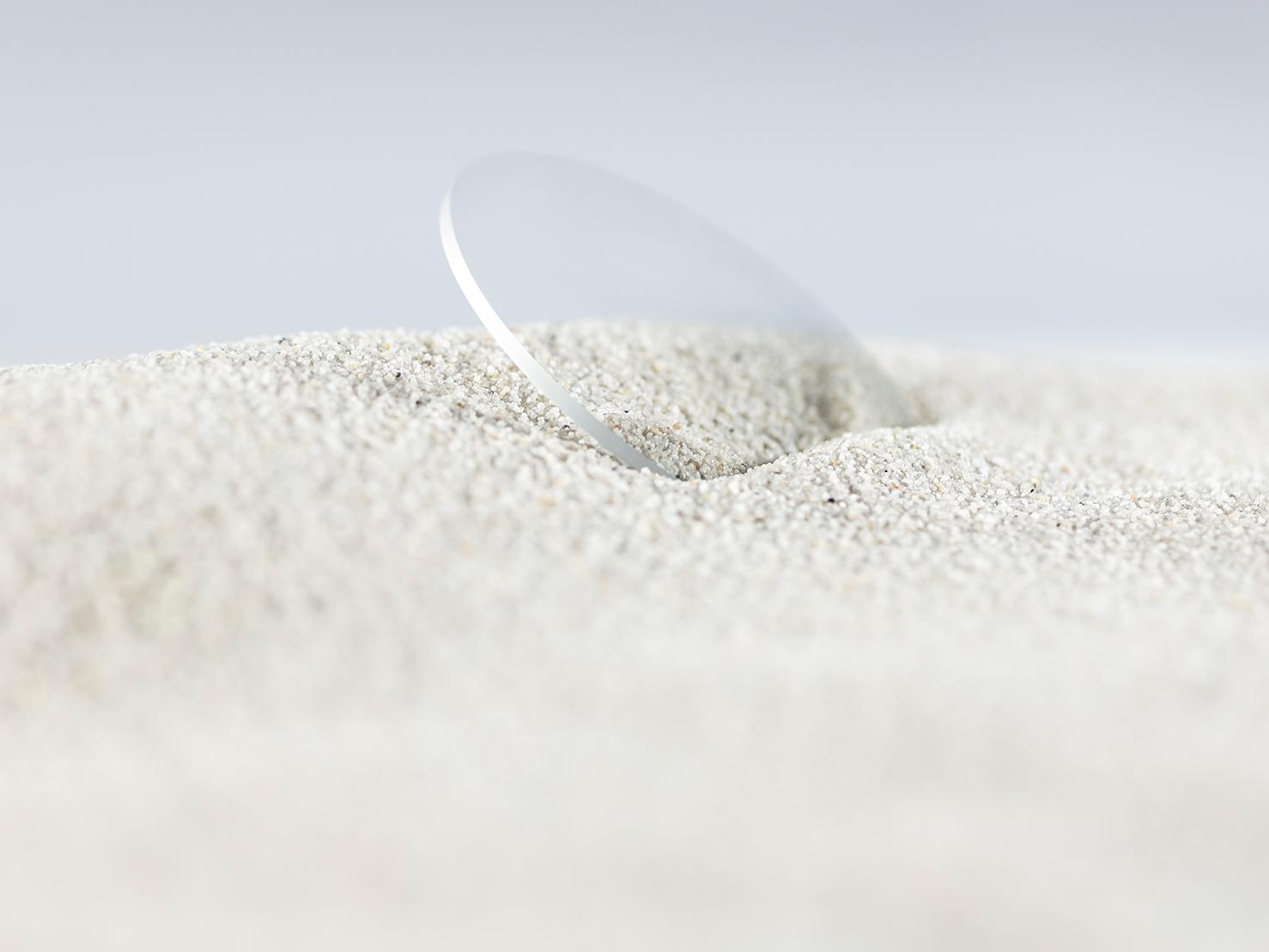 Ein ZEISS Brillenglas mit einer robusten Beschichtung wird von grobem Sand bedeckt und hat trotzdem keine Kratzer.