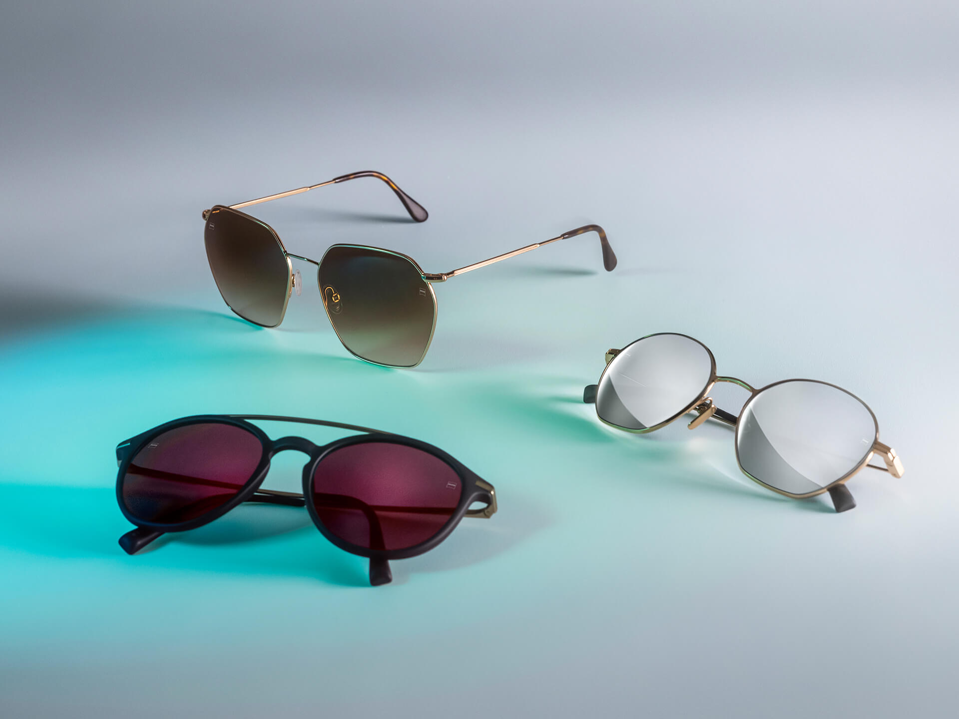 Auf einem weißen Hintergrund sind drei Sonnenbrillen mit verschiedenfarbigen ZEISS Sonnenschutzgläsern mit den Beschichtungen DuraVision Sun, DuraVision Mirror und DuraVision Flash Mirror und Blaulicht-Reflexionen zu sehen.