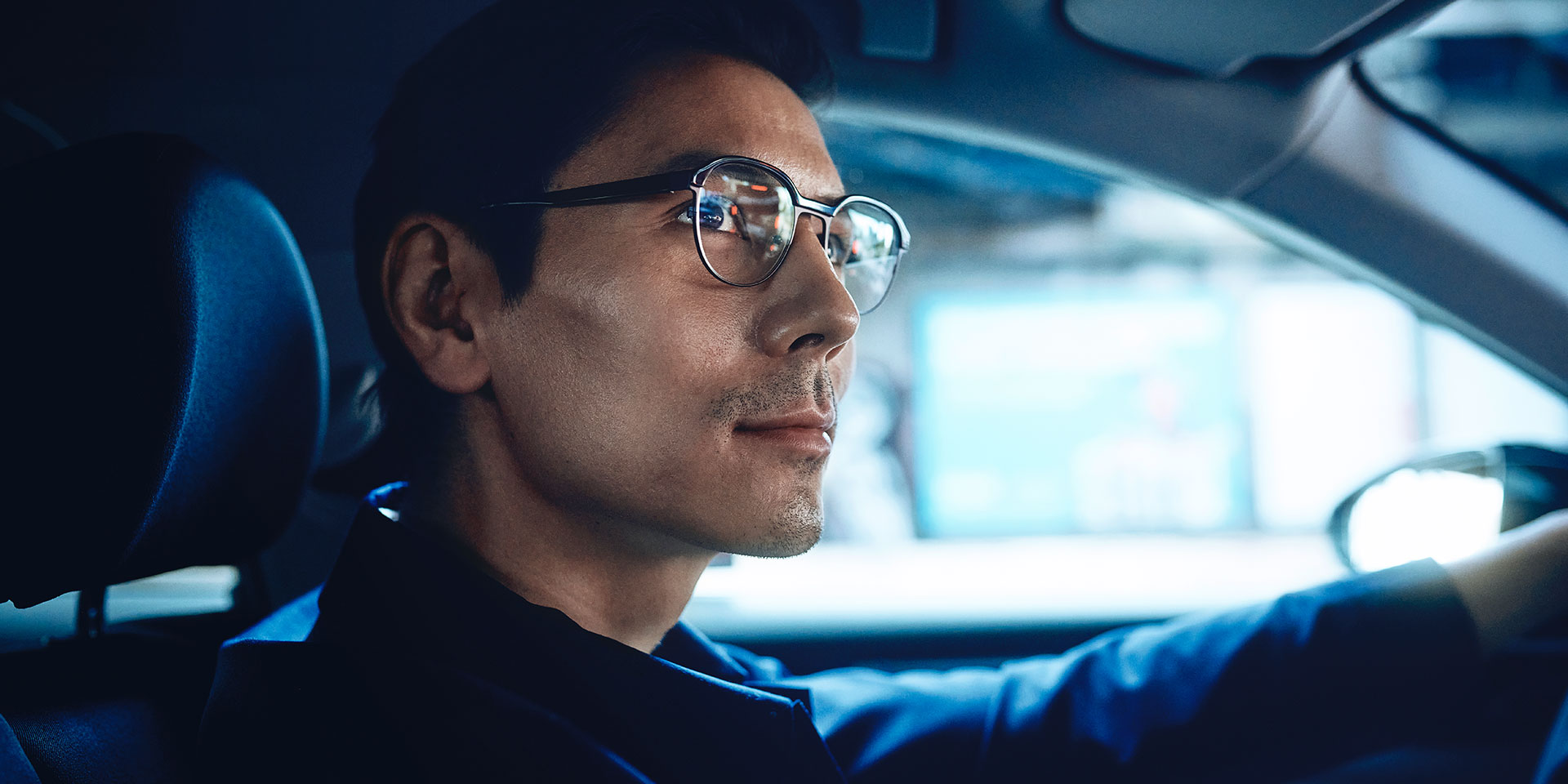 Ein selbstbewusst aussehender Mann fährt Auto und blickt mit einem leichten Lächeln auf die Straße. Er trägt ZEISS DriveSafe Einstärkenbrillengläser.