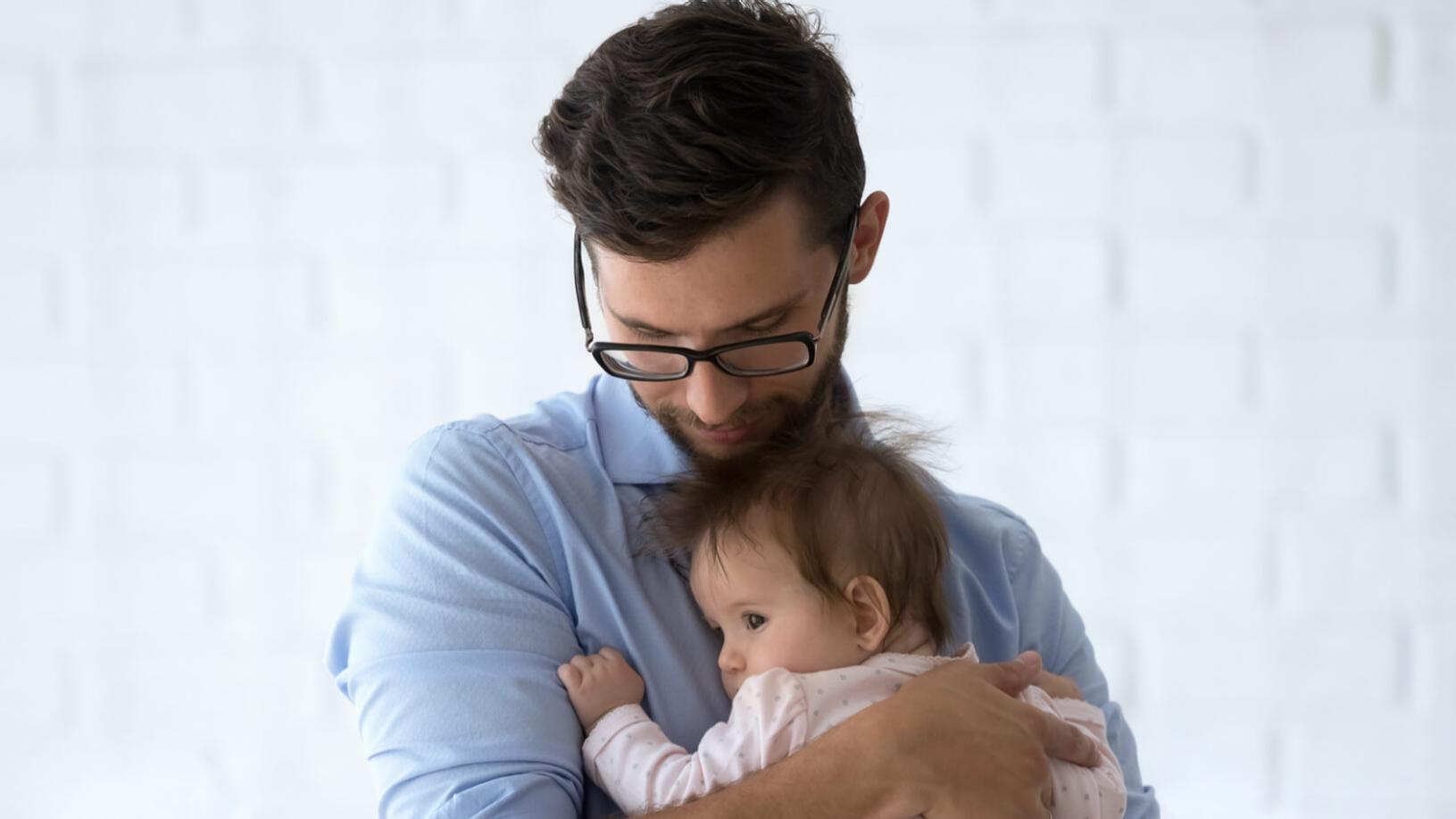 Ein kurzsichtiger Mann mit Brille hält ein Kleinkind im Arm.