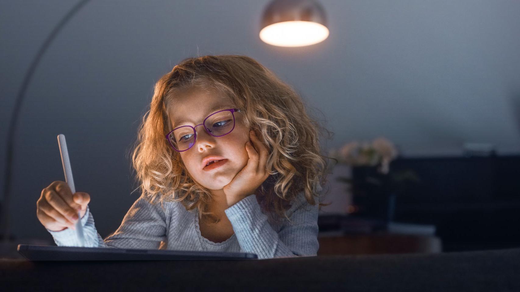 Une petite fille regardant une tablette dans une pièce sombre.