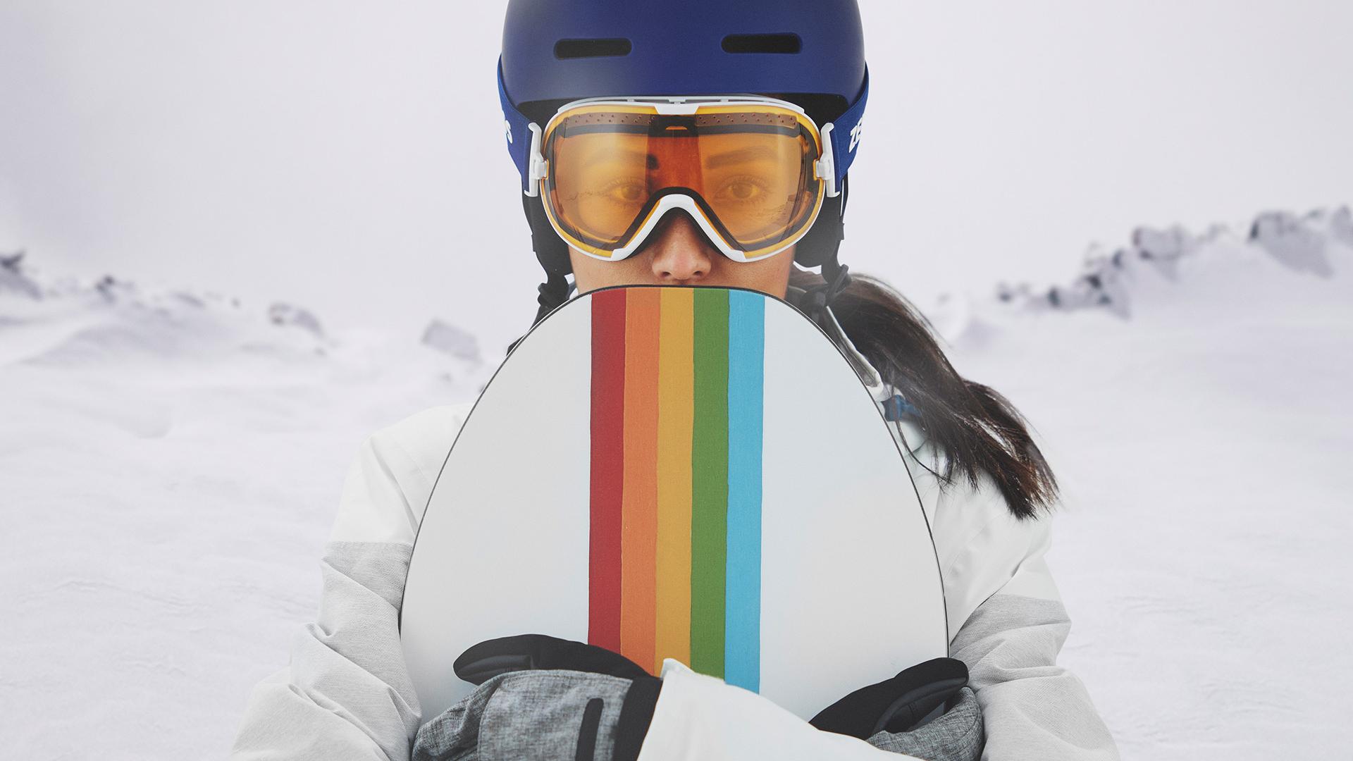 Une jeune femme porte un masque avec la technologie de verres interchangeables ZEISS et tient un snowboard.