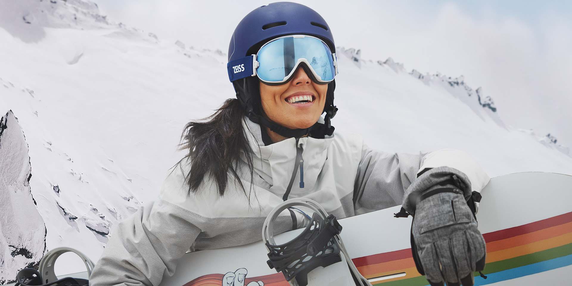 Une jeune femme porte un masque avec la technologie de verres interchangeables ZEISS et tient un snowboard.