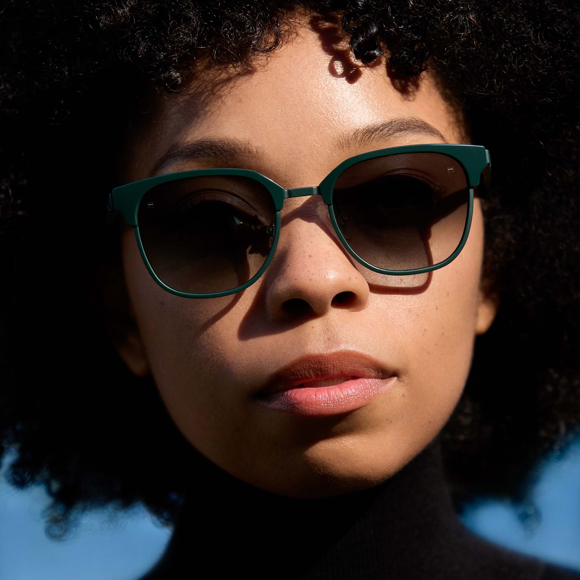 Une femme porte une monture verte avec des verres à teinte dégradée. 