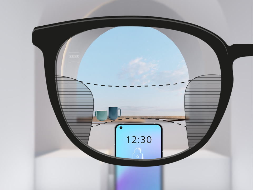 Abbildung mit Blick durch ein ZEISS SmartLife Gleitsichtglas. Ein Smartphone ist zu sehen und im Hintergrund Tassen. Das Brillenglas ist vollkommen klar, mit geringen unscharfen Flächen links und rechts.