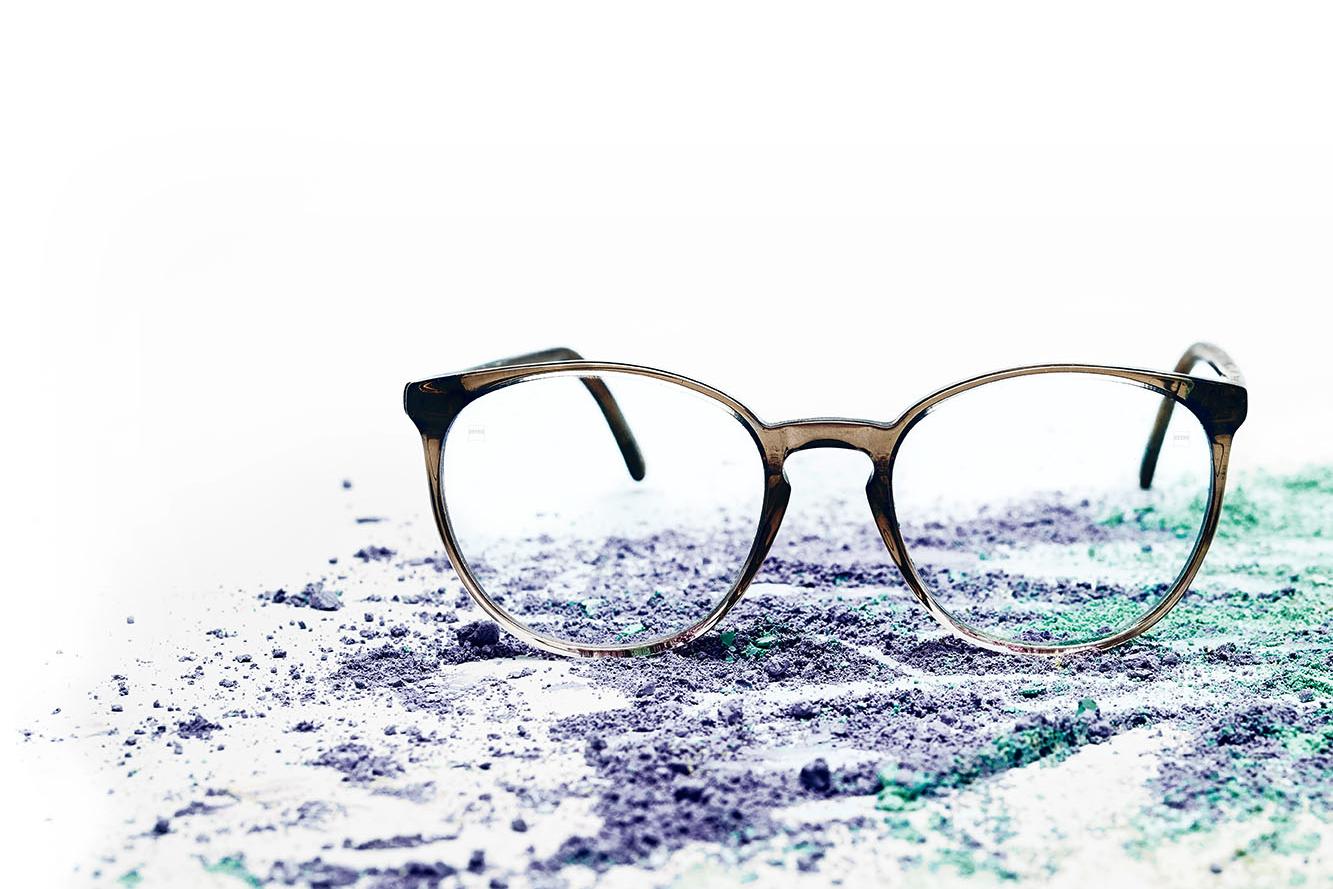 Une paire de lunettes à verres transparents est posée sur de la poudre colorée.