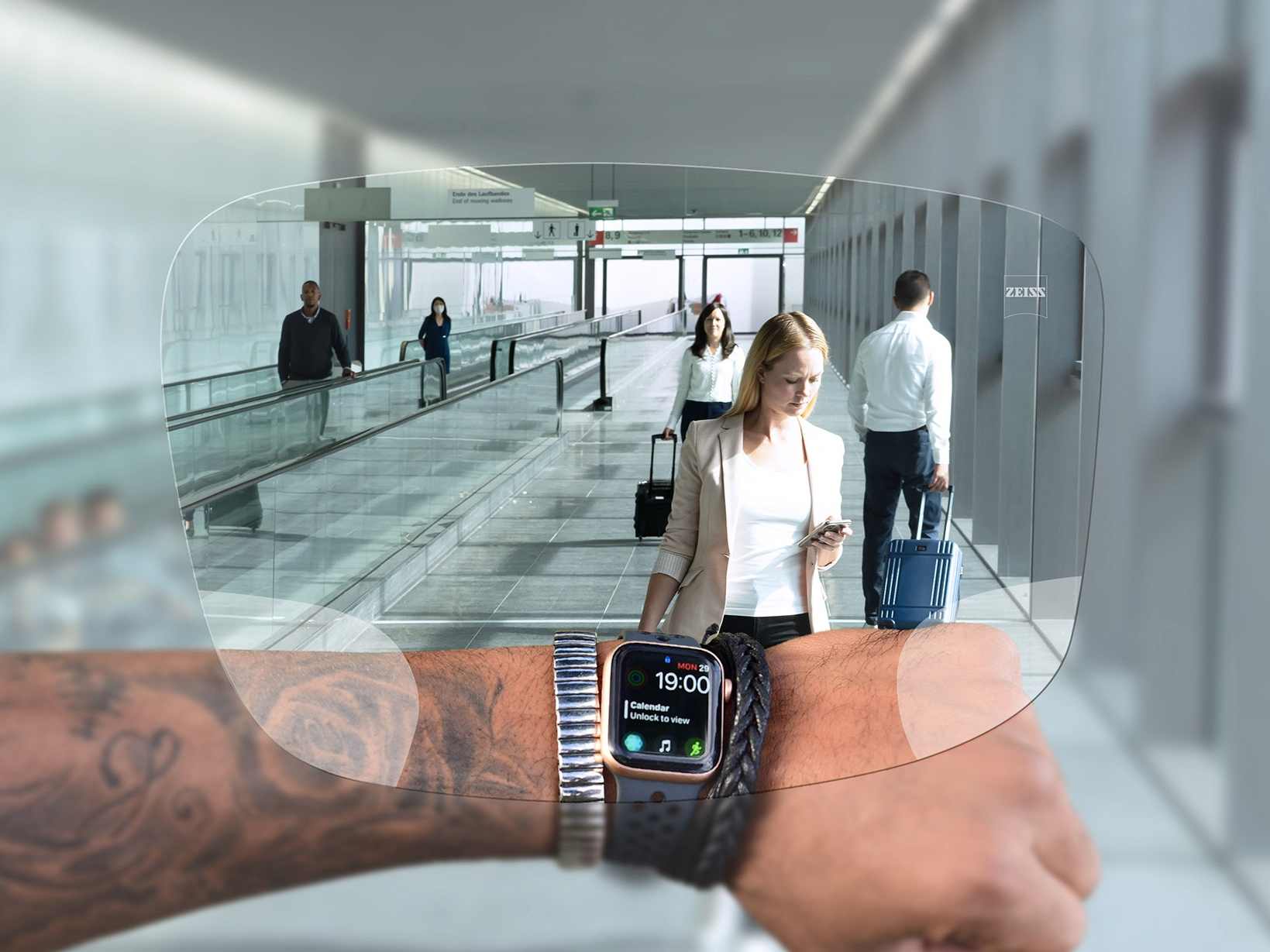 Une personne regarde sa montre à travers des verres ZEISS SmartLife Digital. Une scène d’aéroport typique est visible à l’arrière-plan, avec des personnes sur des escaliers roulants et poussant leurs valises. 