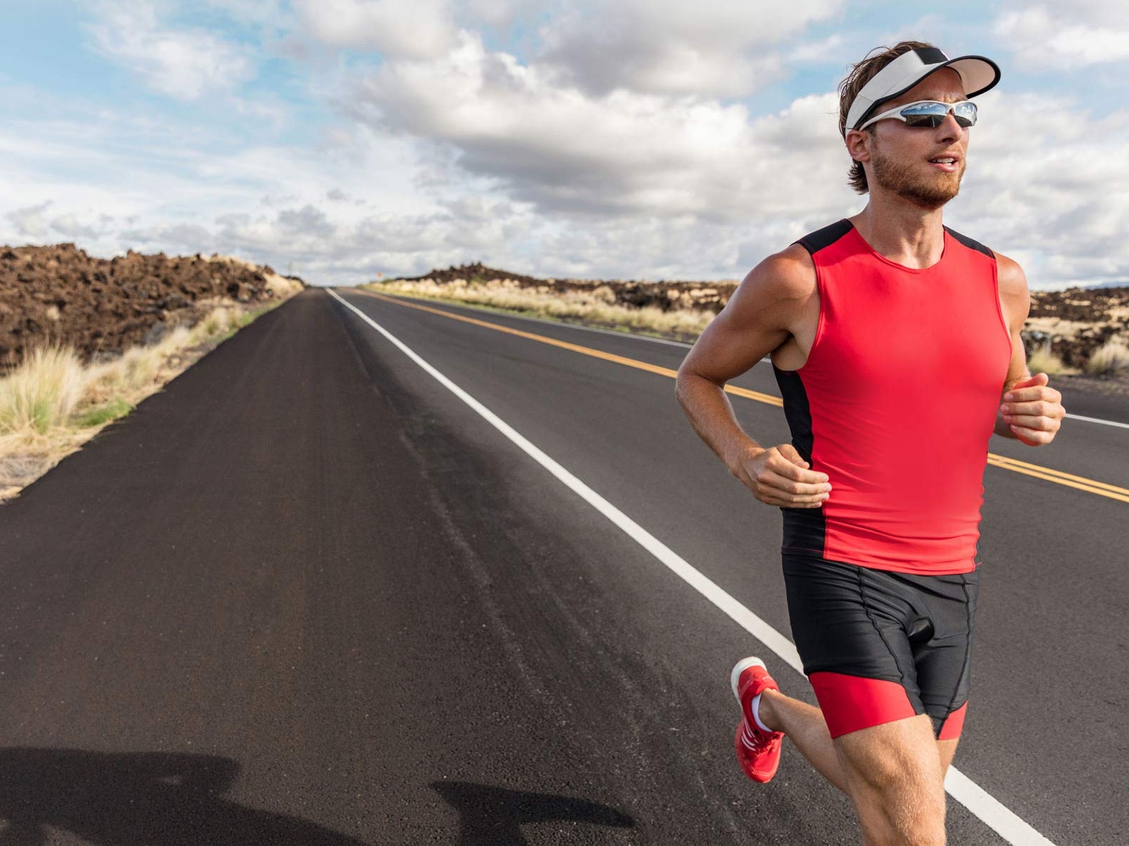 Une image d’un homme portant des vêtements de sport et des verres sportifs en train de courir sur la route. 